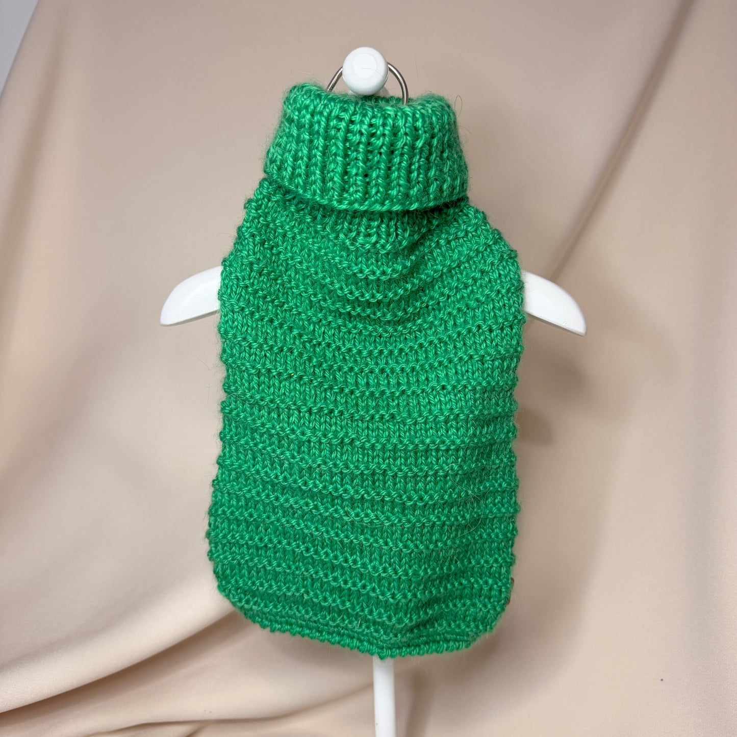 Green knitted dog sweater on a hanger against a beige background